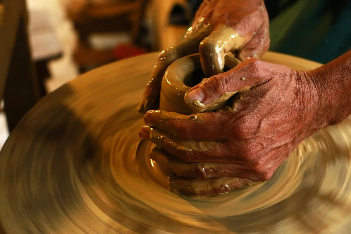 Close-up of anonymous hands polishing a crystal object on a workbench, workshop tools and protective gloves blurred in background