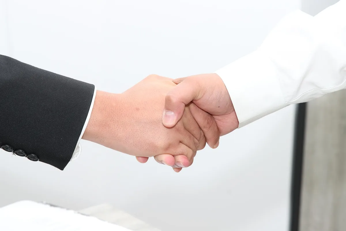 Hands pointing at a simplified M&A flowchart on a desk, documents and a closed laptop visible
