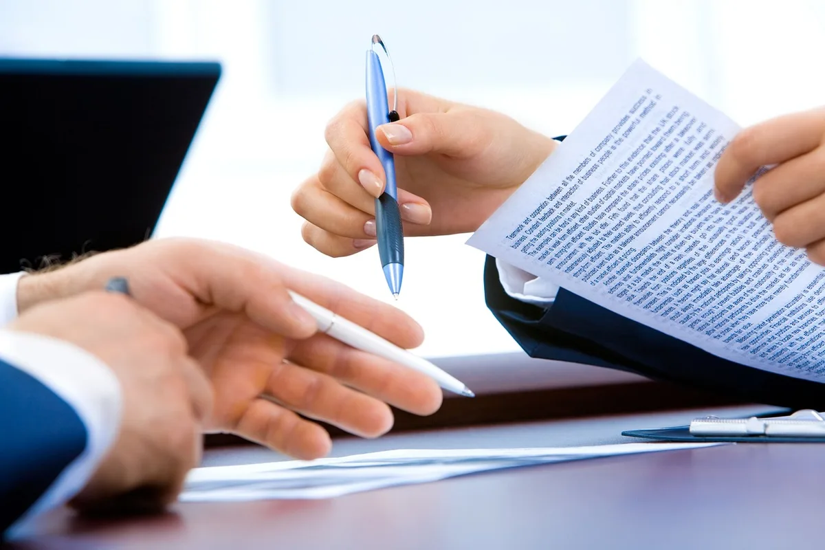 Well-lit desk with hands holding a printed ranking page, a pen, and a closed laptop; no logos, no faces