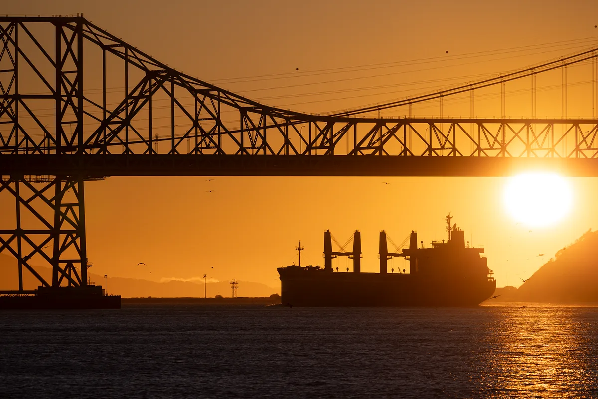 Empty tanker lane at sea near a narrow strait, distant unbranded cargo ships, calm water under clear sky, no people visible