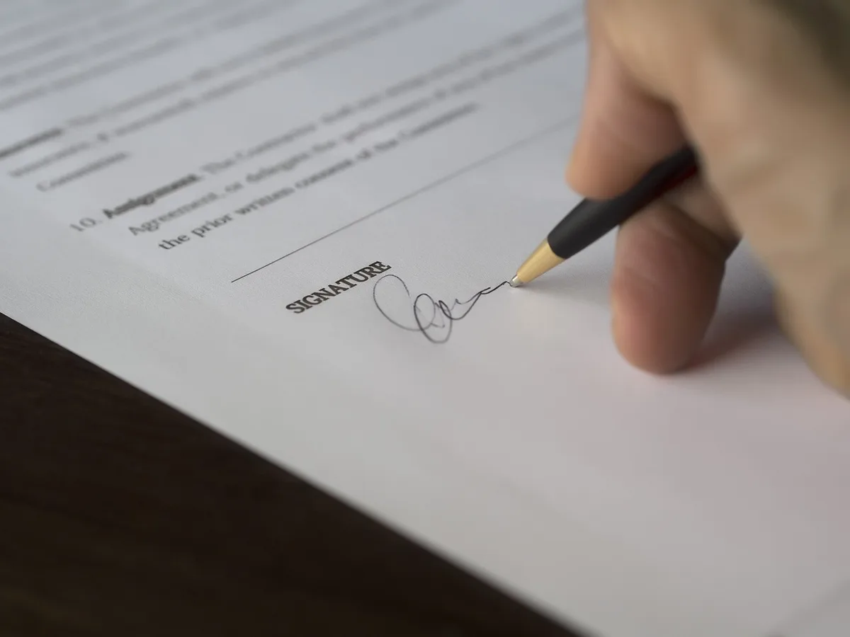 A desk with application forms, a calculator and a pen, hands filling fields on a form