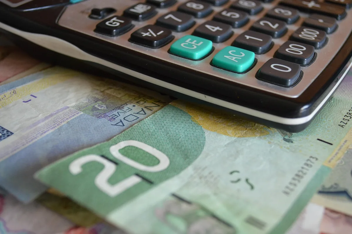 Close-up of a calendar and a bank statement beside a laptop showing a budget spreadsheet