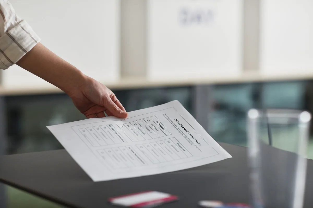 A clean desk with university notes, a pen and a printed survey form showing checkboxes, hands holding a pen over the page