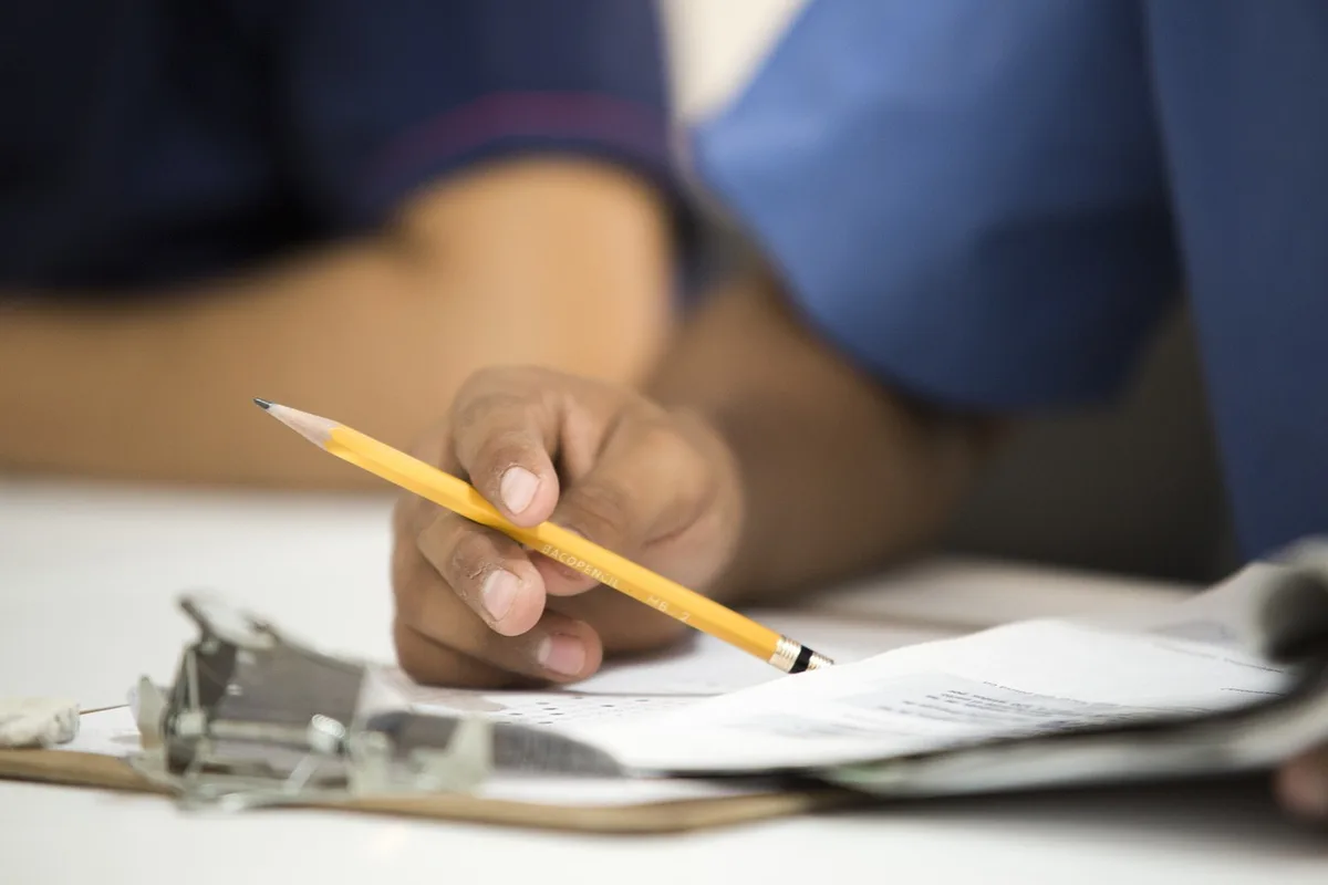 A well-lit office desk with hands filling out an apprenticeship contract form, a laptop open and a printed checklist nearby
