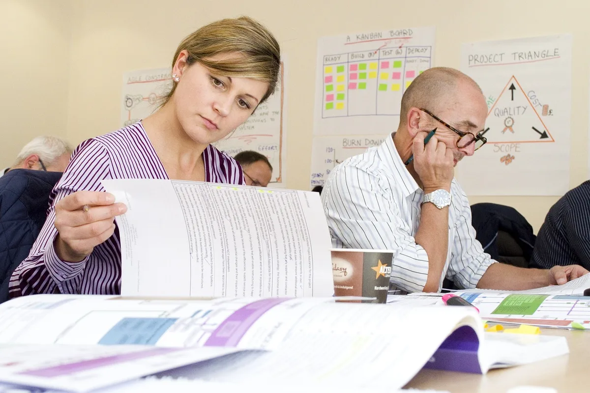 hands filling a certification checklist on a desk with printed guidelines visible but unreadable