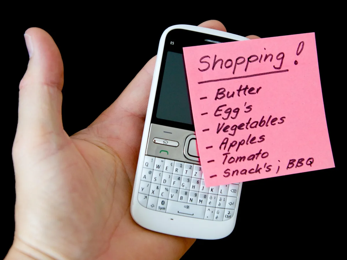 Close-up of hands pointing at a printed PDF table of names, a smartphone nearby showing a government site
