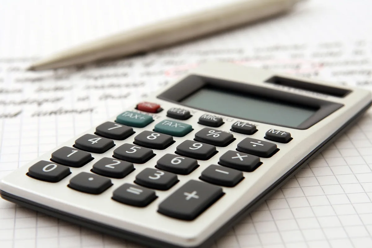 Close-up of hands filling a government pension form on a wooden desk, a stamped envelope and a calculator slightly blurred in background