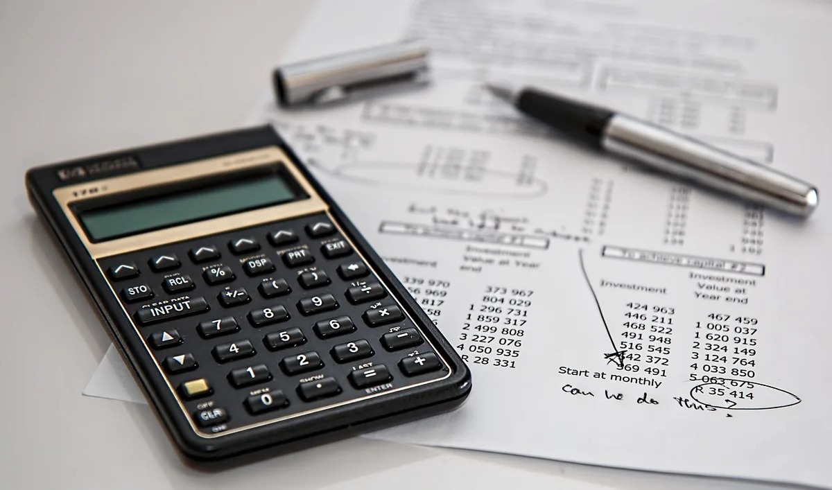 A tidy desk with a printed bank list, generic finance books, a notepad with division names handwritten and a cup of coffee